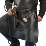 Nero Vulcano — Men's Jet Pitch Black Genuine Thick Heavy-Duty Rubber-Toughened Full-Grain Cowhide Leather Welding Forge Apron Adjustable Snap-Button Shoulder Strap Contrast Tan Stitch Wide Flared Lower Skirt Panel Side Torch Holder Tool Loop Brush Pocket Welder Blacksmith Farrier Foundry Forge Craftsman Industrial Heavy Workshop Utility Apron - Image 2